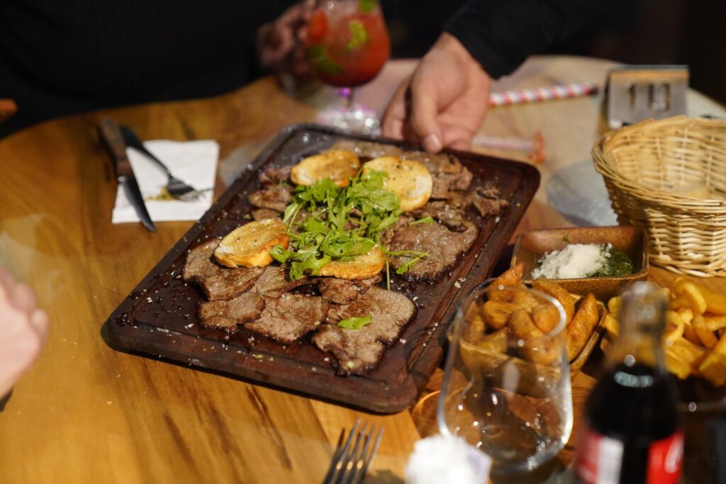 Planche de bœuf grillé servie en salle avec roquette et croûtons