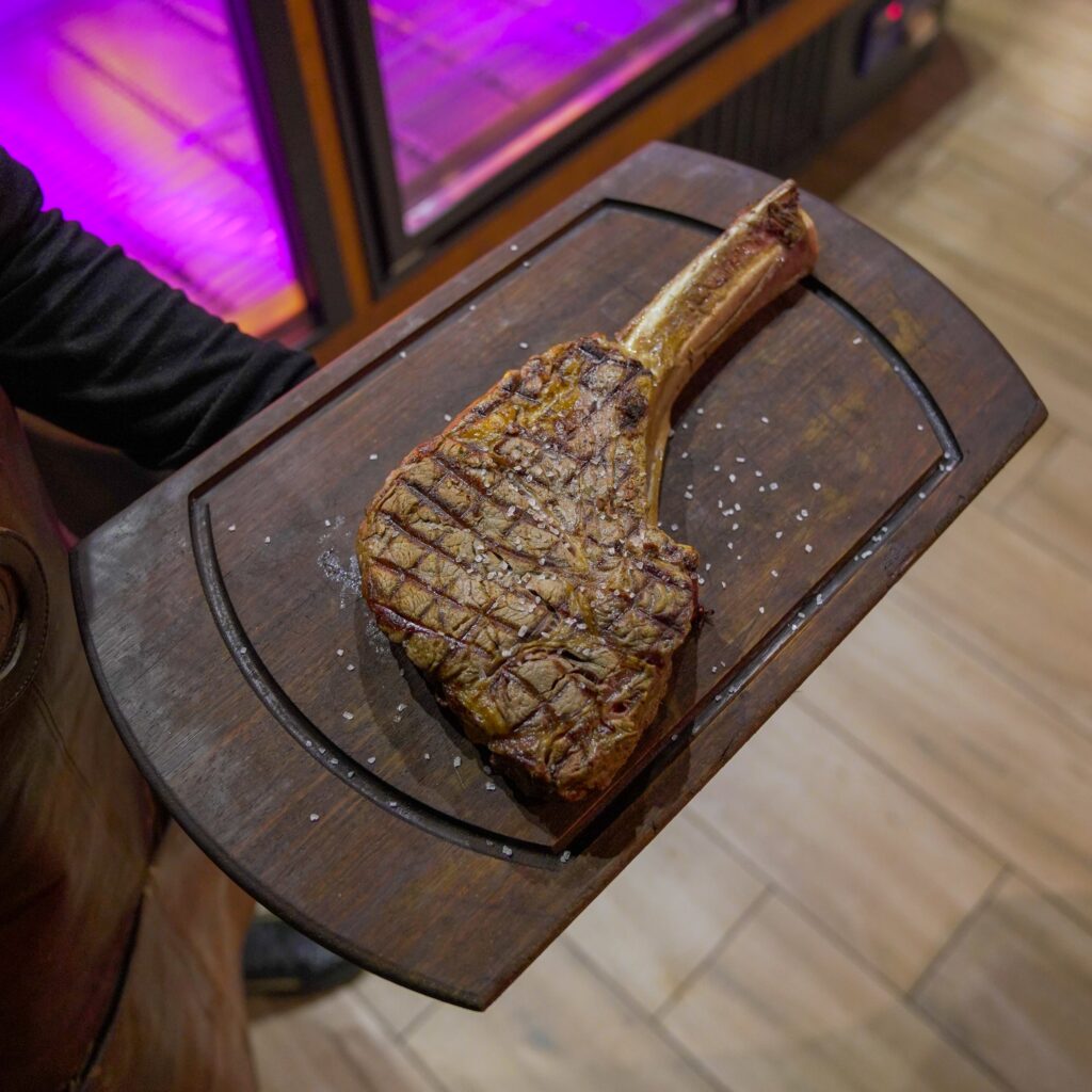 Tomahawk grillé présenté sur planche en bois par le serveur